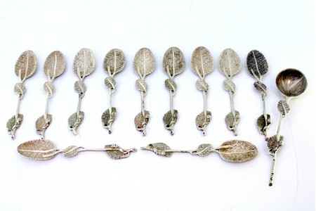 Conjunto de seis colheres e pá de açúcar em prata com cabos relevados e conchas em forma de folhas com nervuras.